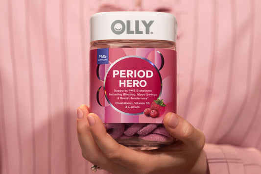 Hand holding a jar of Olly Period Hero supplement with a pink background