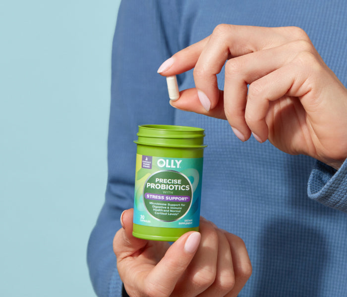 Woman holding OLLY Precise Probiotics bottle and capsule