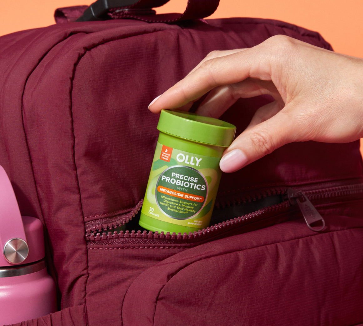 Hand placing a container of Olly Precise Probiotics into a maroon bag with a pink thermos.