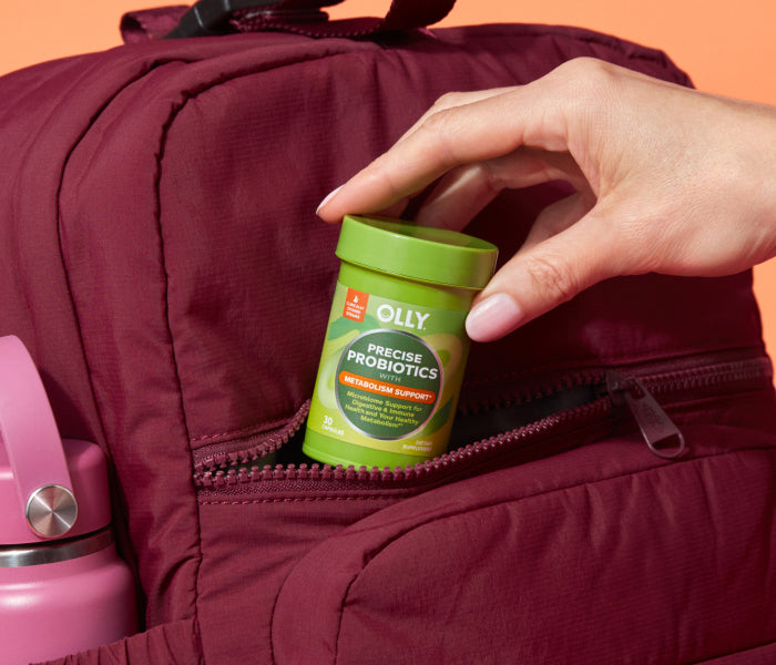 Hand placing a container of Olly Precise Probiotics into a maroon bag with a pink thermos.